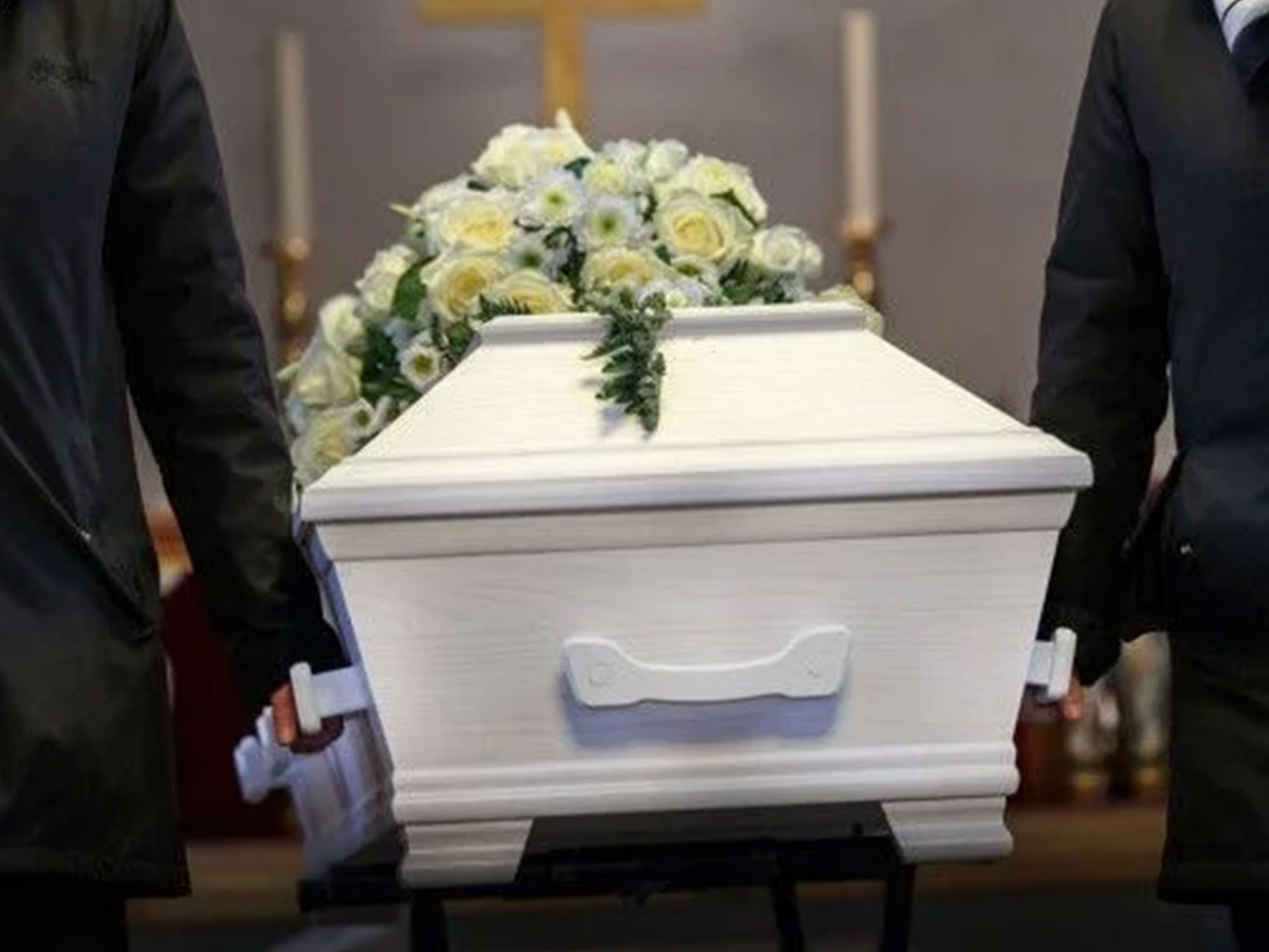 To personer bærer en hvid kiste dekoreret med hvide og gule blomster.