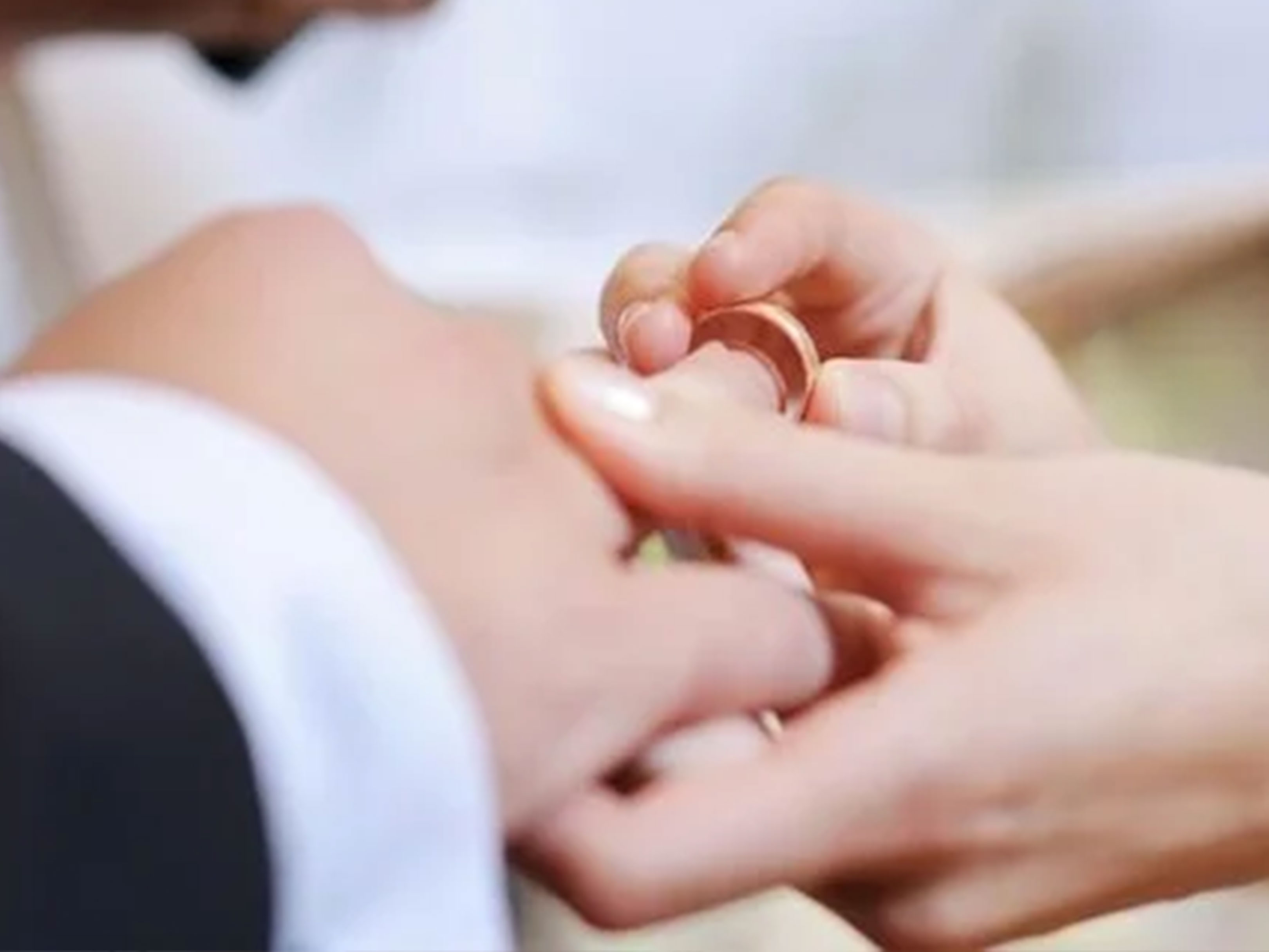 Nærbillede af en person, der sætter en guld vielsesring på en anden persons finger.