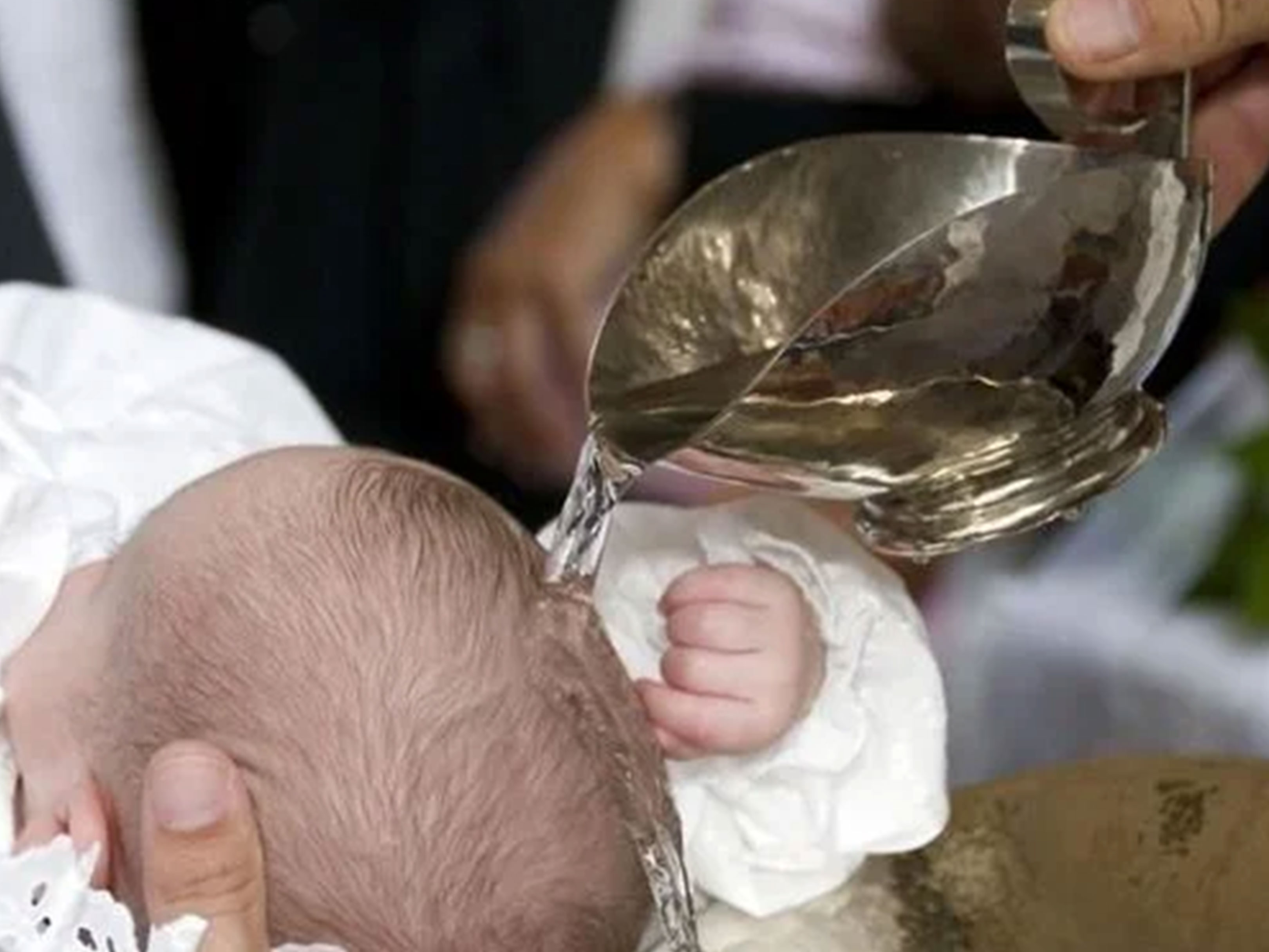 Vand hældes fra en sølvkande over hovedet på en baby under en dåbsceremoni.