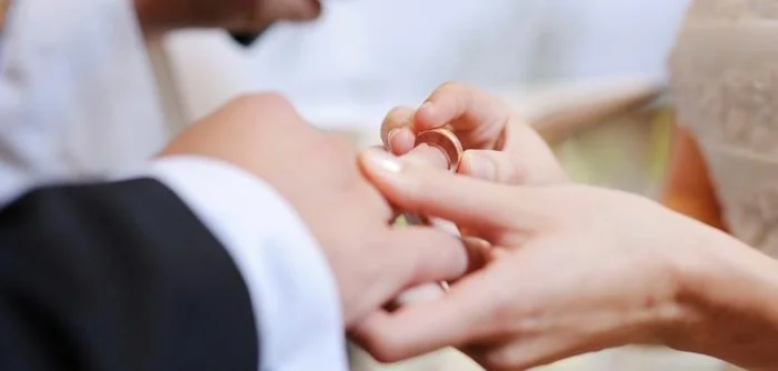 Nærbillede af vielse, hvor bruden sætter ring på gommens finger.